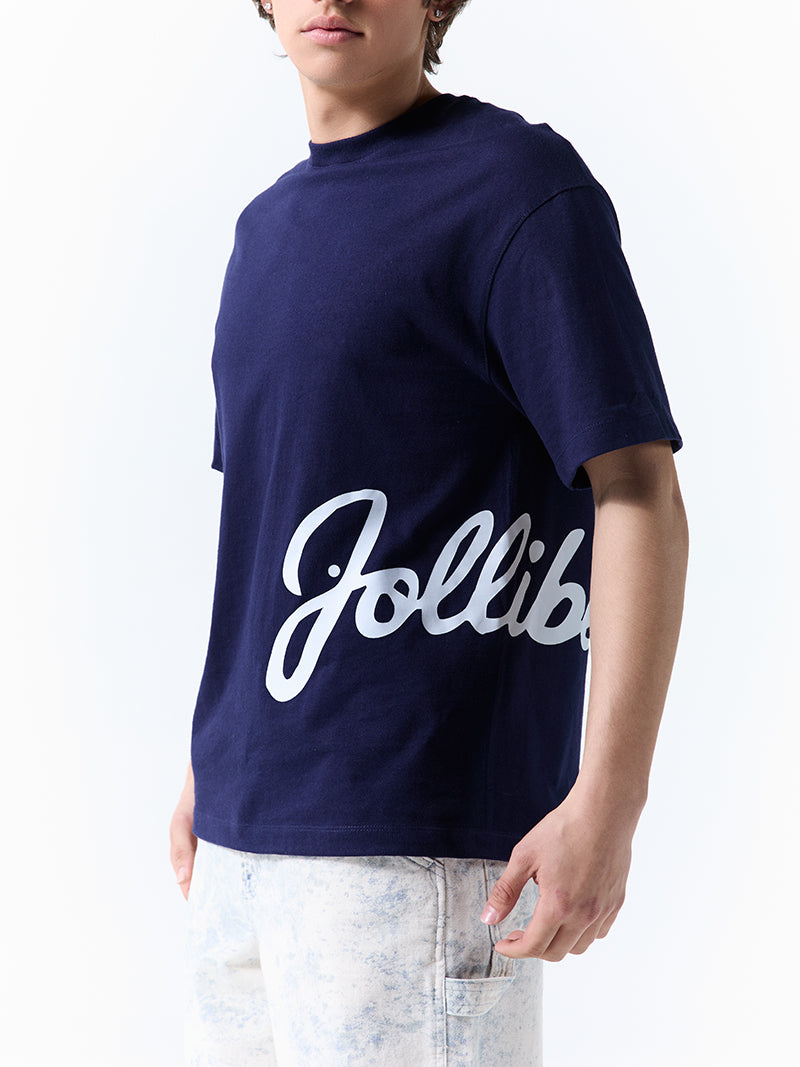 A young man wearing a navy t-shirt with 'Jollibee' in script on the side on a white background.