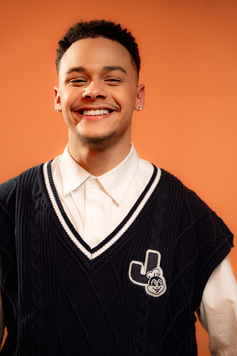 Person wearing a black sweater vest with a logo on an orange background
