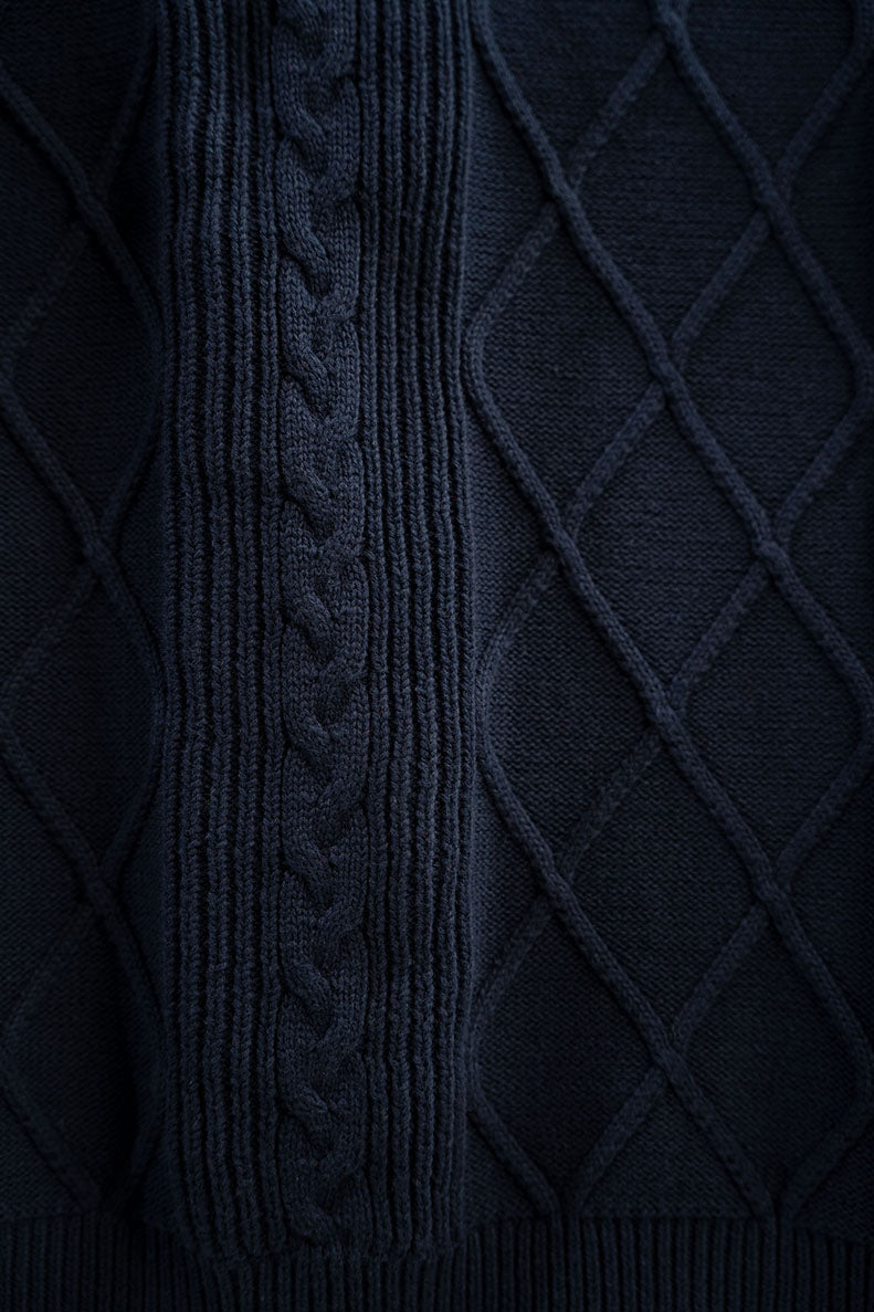 Close-up of a navy blue sweater with intricate cable knit pattern