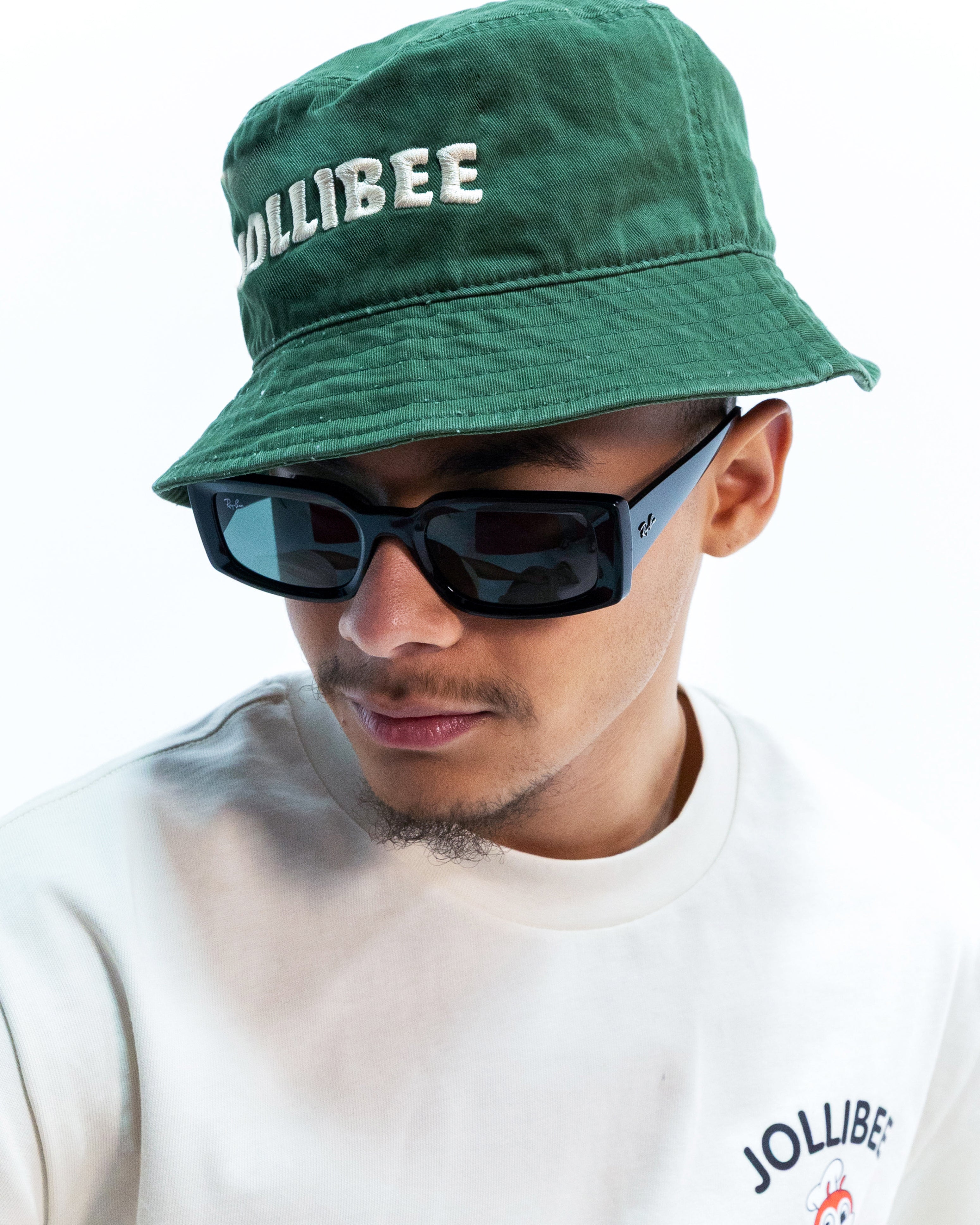 Person wearing a green 'Jollibee' hat and sunglasses with a white shirt.