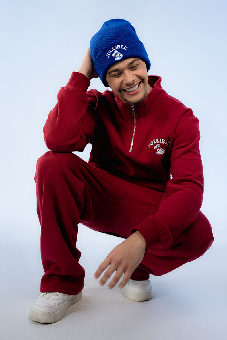 Person wearing a red tracksuit and blue beanie with visible Jollibee logo on a white background