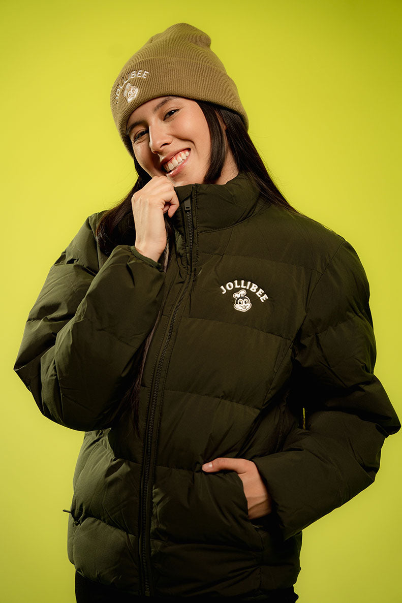 Person wearing a puffer jacket and brown beanie with a Jollibee logo on a yellow background