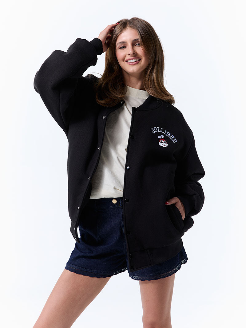 Woman wearing a black varsity jacket with a logo on a white background