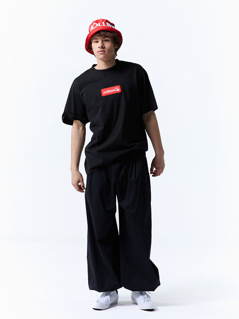 Person wearing a black t-shirt with a Jollibee red logo and wide-leg pants on a white background