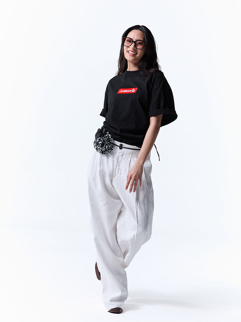 Woman wearing a black t-shirt with a red logo and white pants on a white background