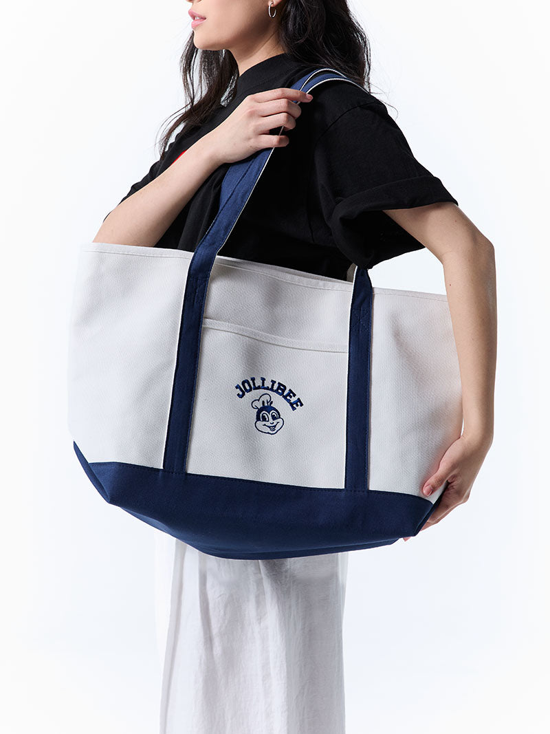 Person holding a white tote bag with navy accents featuring a Jollibee logo, against a white background.