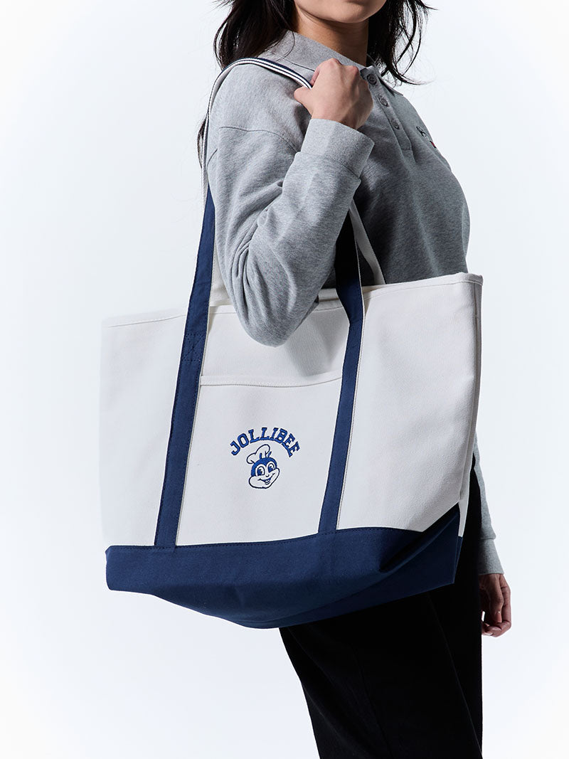Person holding a navy and white tote bag with 'Jollibee' branding on a white background