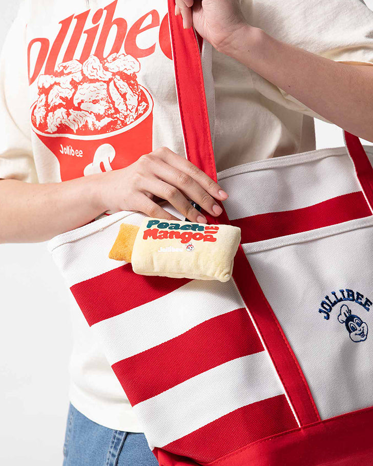 Person holding a Jollibee branded bag with a Peach Mango Pie plush charm, wearing a matching shirt.
