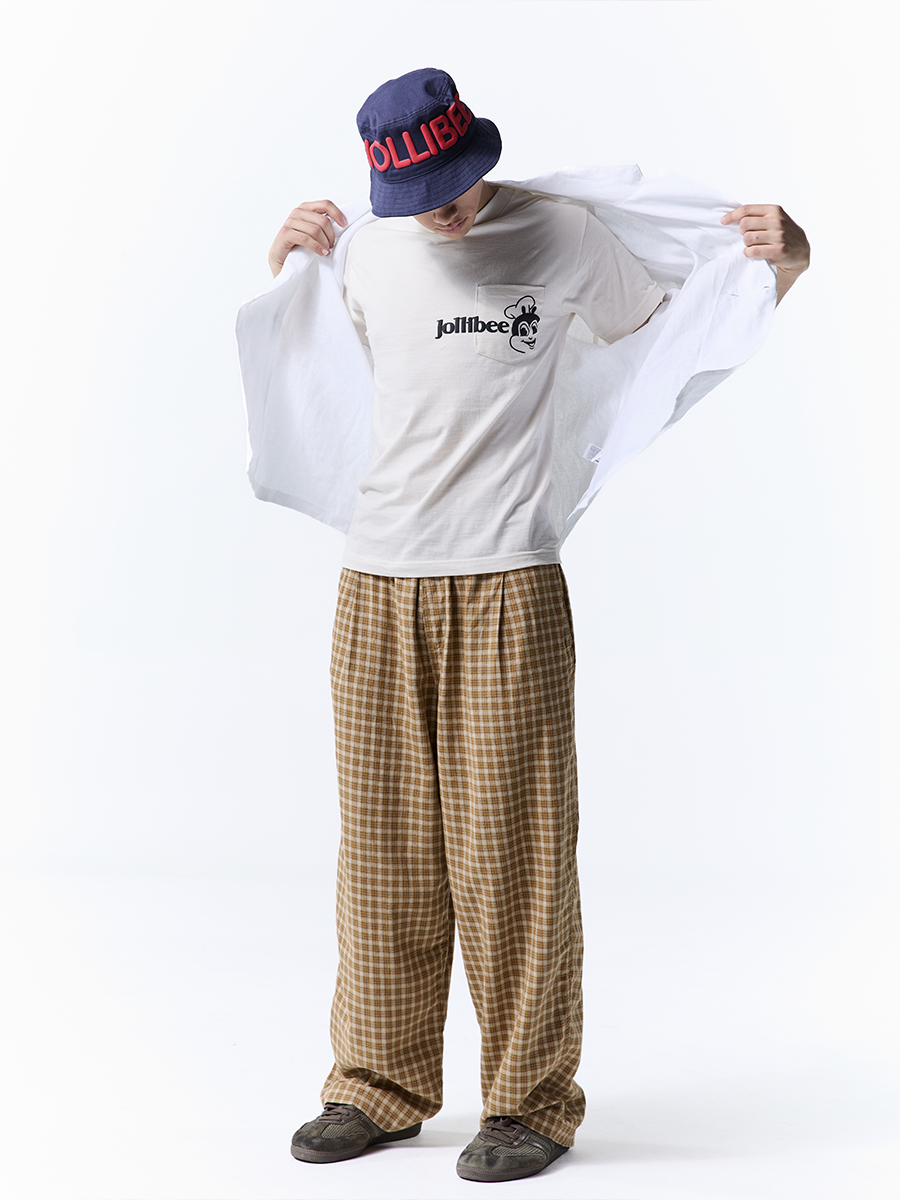 Person wearing a beige shirt with a logo, plaid pants, and a cap on a white background